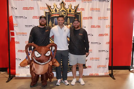 Three men and an inflatable bug mascot in front of the Kingdom Clash backdrop