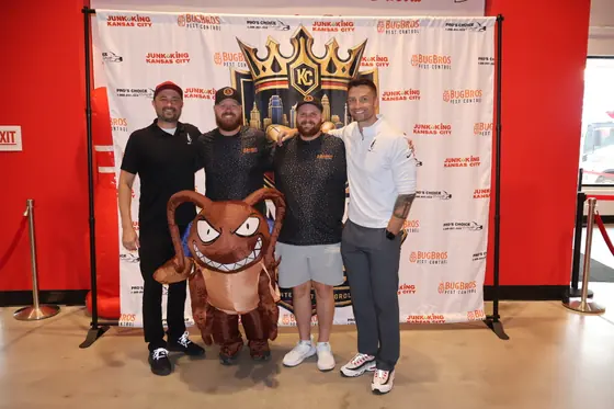 Four men and an inflatable bug mascot in front of the Kingdom Clash backdrop