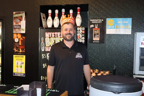 A smiling vendor beside a shelf of bowling pins
