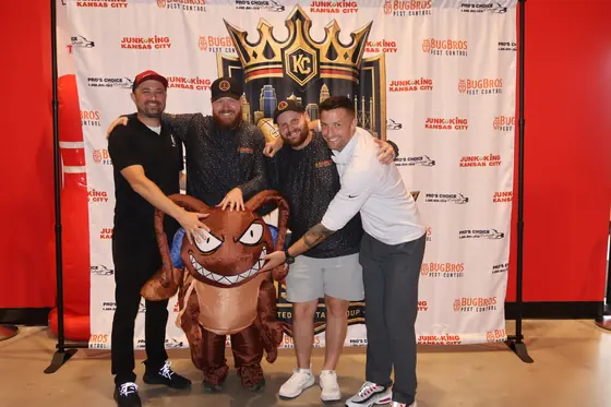 Four men and an inflatable bug mascot in front of the Kingdom Clash backdrop